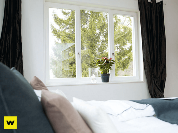 Helles Schlafzimmer mit großem Fenster, blick ins Grüne, Pflanze auf Fensterbank.